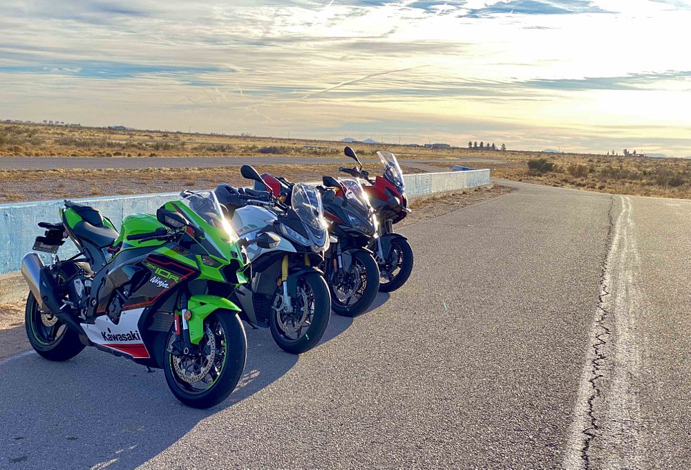 group image of four motorcycles parked near a racetrack