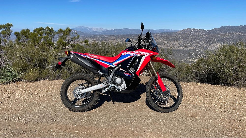 A side view of the bright red Honda CRF300L Rally dual sport motorcycle on a dirt trail