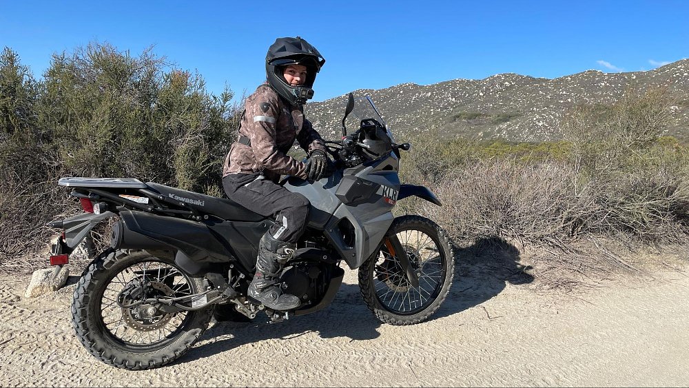 A female rider sits on the KLR650 S with a. mountain view and a smile on her face