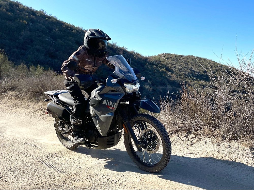 A female rider is riding the KLR650 S motorcycle on a dusty truck trail road