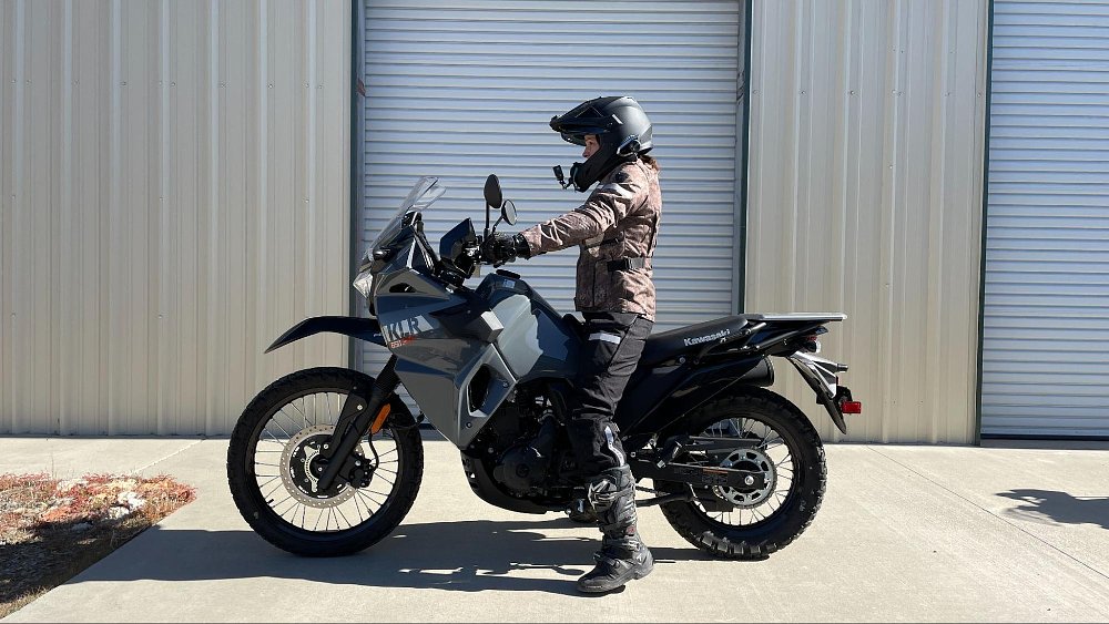 A short female rider sits on the lowered KLR650 S motorcycle with her feet touching the ground