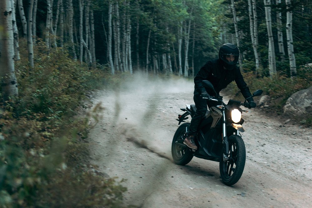 A rider is flat tracking around a dirt road corner throwing roost on an electric Zero DS bike