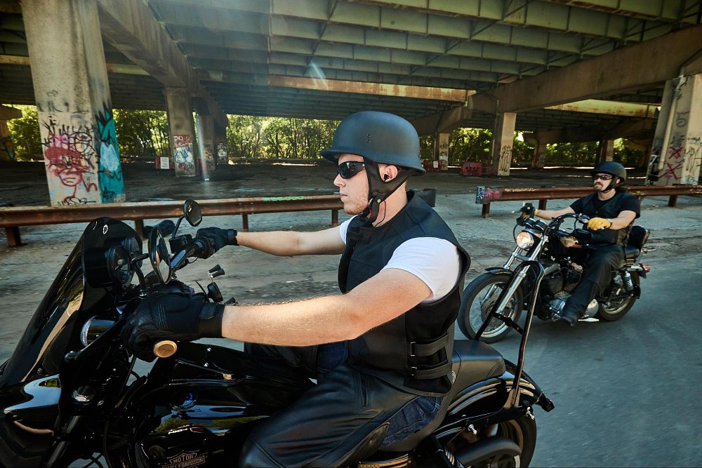 a photo of two cruiser motorcycle riders riding under a bridge wearing half face helmets