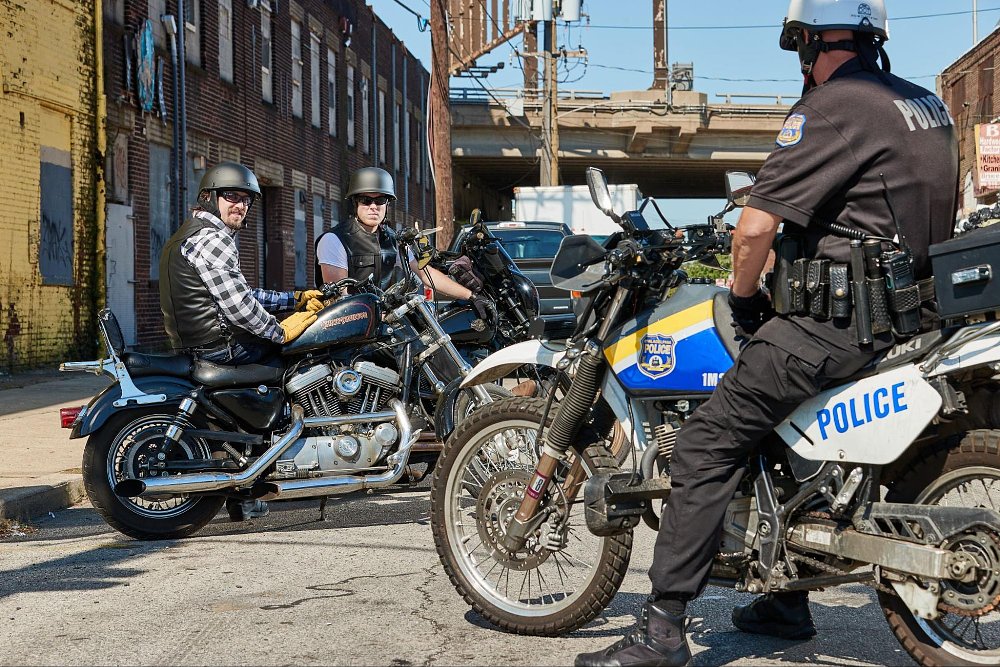 two motorcycle riders in a alleyway interacting with a police cop