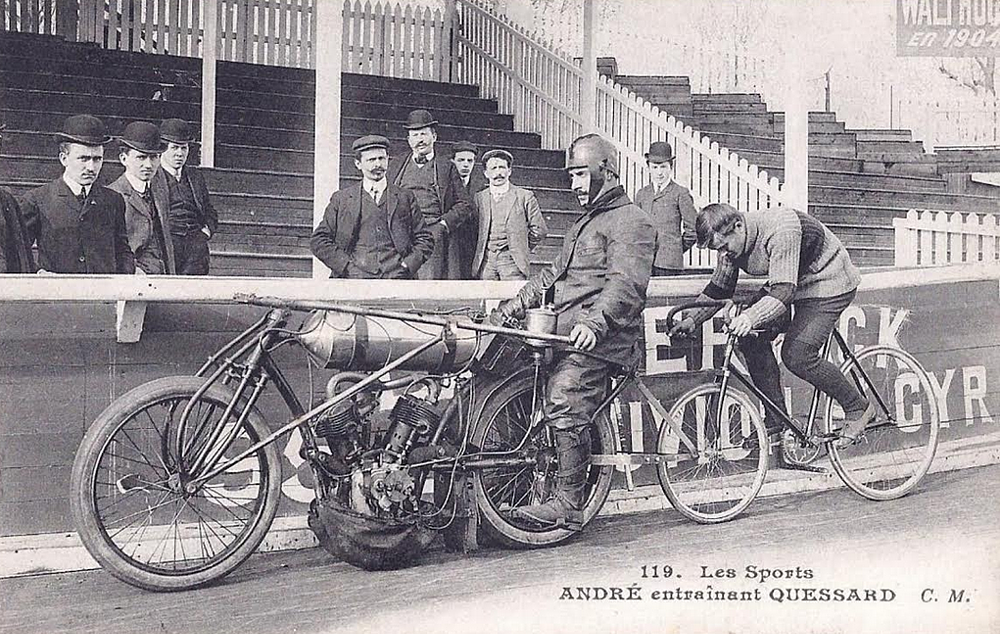 a vintage photo of a motorcycle hooked up to tow a bicycle in a velodrome race