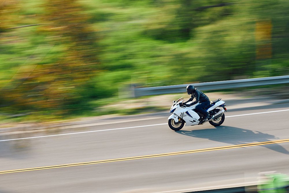 2023 Suzuka Hayabusa riding right to left with a blurred green background.