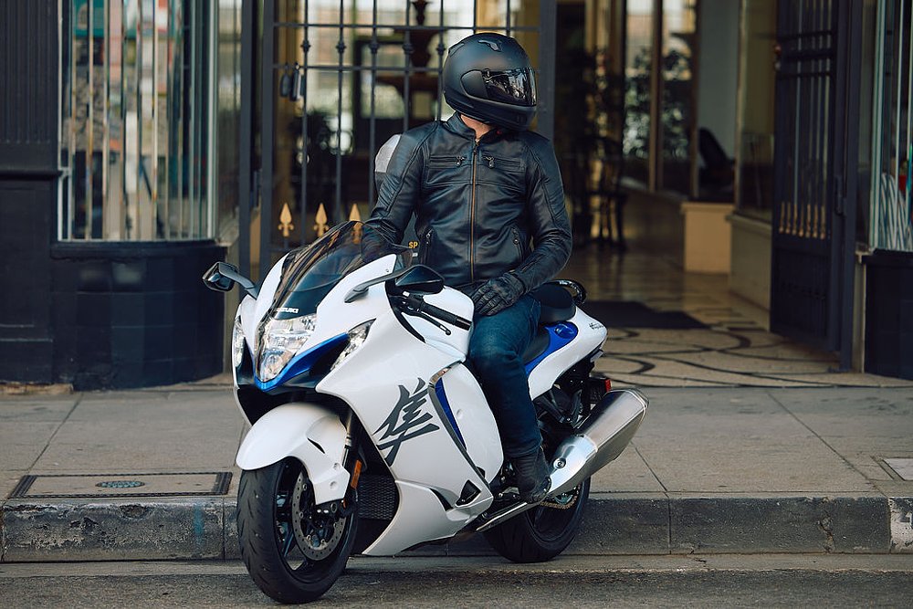 2023 Suzuki Hayabusa left side, parked at a curb with a rider looking over their left shoulder.