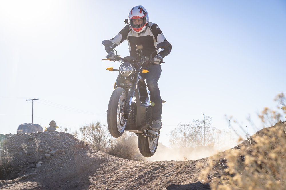 A Sondors Metacycle jumping over a dirt mound on a desert trail.