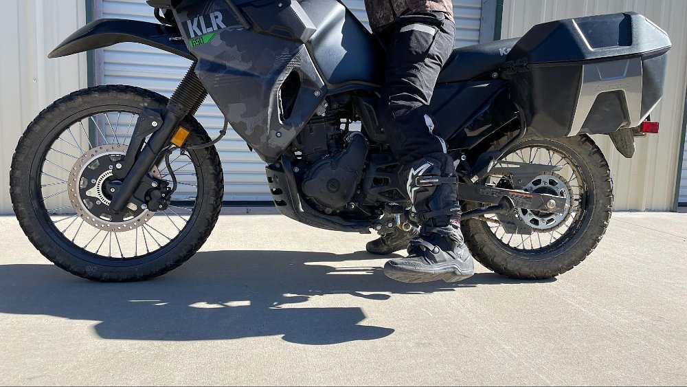 a close up of riders feet dangling trying to touch the ground on a kawasaki KLR650 adventure bike