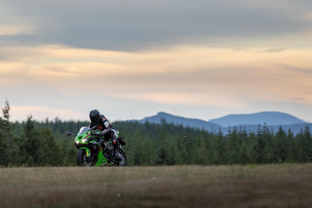 A far away shot of the kawasaki ninja zx-6r riding on a racetrack with dusk and pine trees