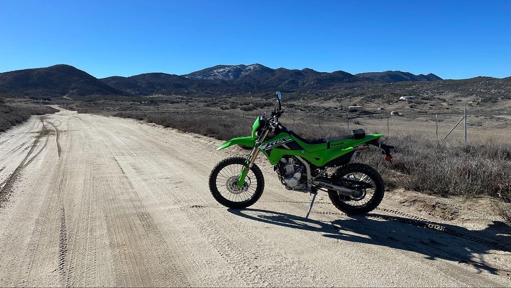 The KLX300 parked on the side of a smooth dirt road into a hillside