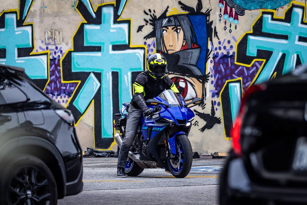A rider on a 2024 Yamaha R1 pausing to leave a parking lot in Los Angeles's Japantown, with graffiti in the background.