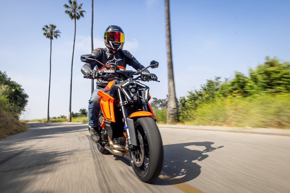 A KTM 1390 Super Duke R riding down a narrow road lined with palm trees.