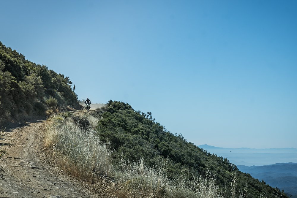 2024 BMW R 1300 GS riding along a dirt road with a view of hilltops to one side.