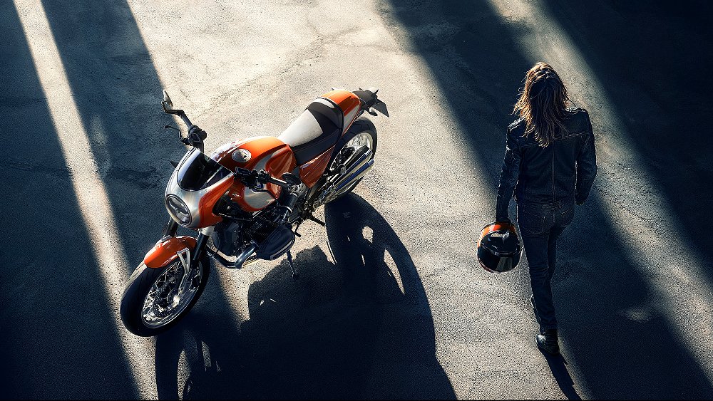 A stylish female rider walks up to a parked BMW R 12 S.