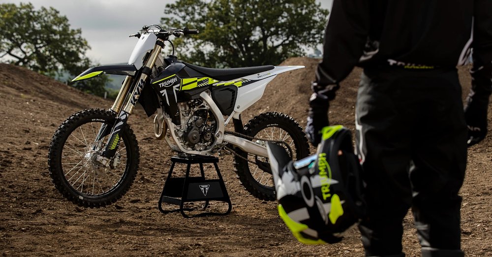 view of rider from behind looking at a Triumph TF250-X motocross bike on a stand at an MX track