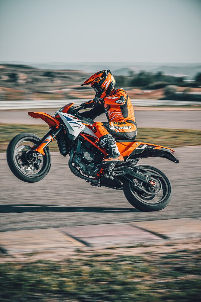 A KTM 390 SMC R rider performs a wheelie on the track.