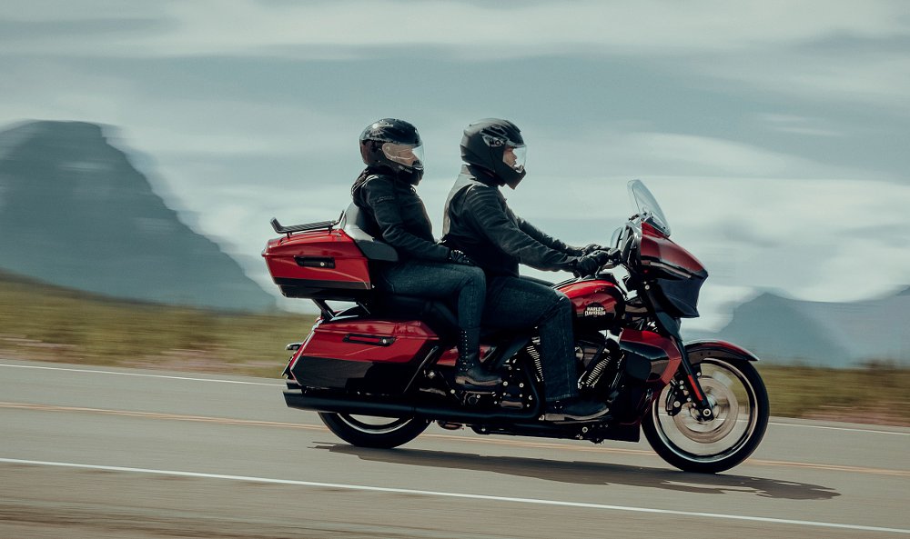 rider and passenger on a red and black Street Glide Ultra in front of a lake and mountains