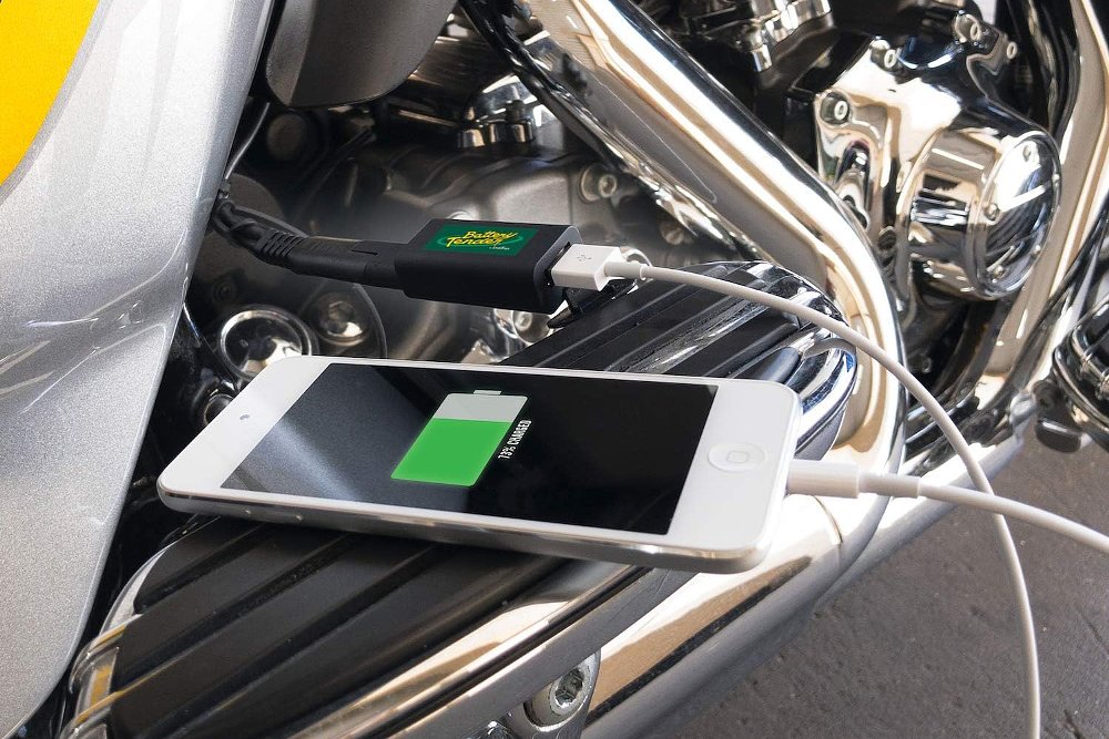 A close-up of an iPhone charging via a USB cable connected to a motorcycle battery lead.